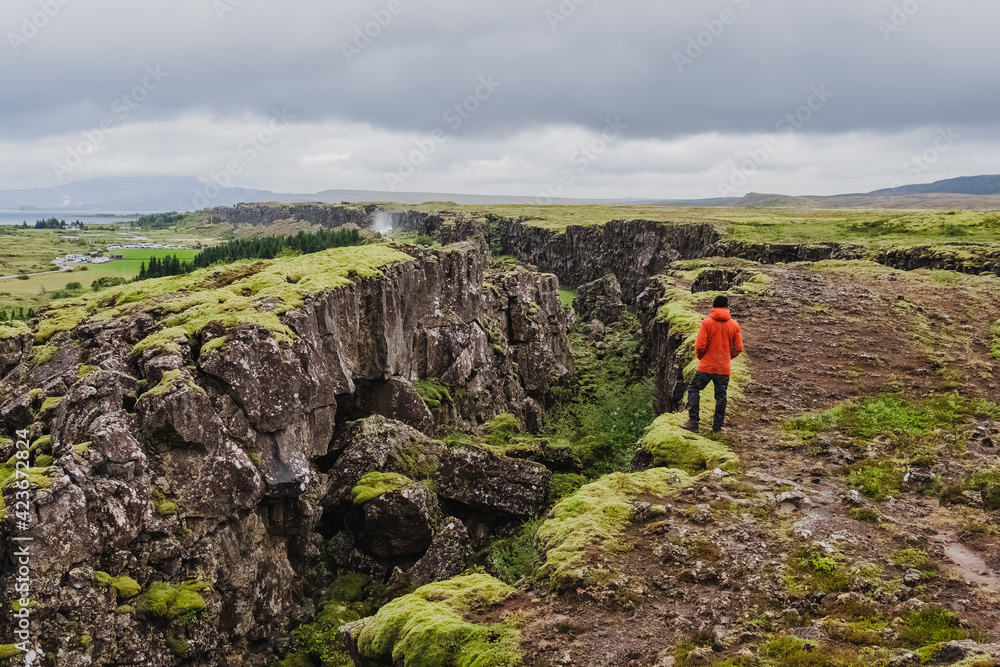 A man in a red jacket stands in Tingvelir National Park in Iceland. Fracture of tectonic plates. Panoramic photo. It is the site of a rift valley that marks the crest of the Mid-Atlantic Ridge. 