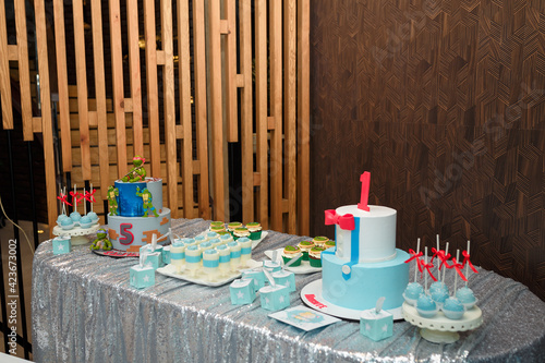 Festive candy bar for 1 and 5 years old boys birthday party. Cake with red number 1 and butterfly bow on shirt. Blue cakepops, cupcakes with red bows and Teenage Mutant Ninja Turtles.