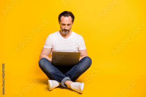Full size photo of serious focused mature man sit floor work online freelancer isolated on yellow color background © deagreez