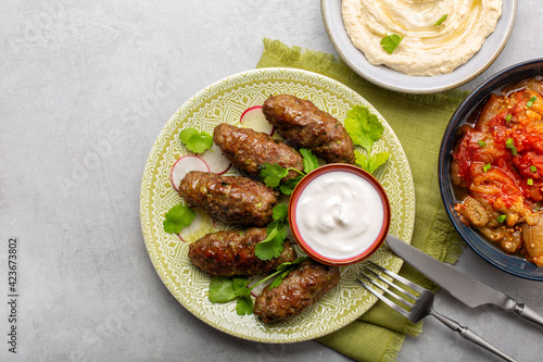 Middle eastern food. Beef koftas with yogurt,  hummus and baked aubergines with tomatoes. Grey background. Copy space.