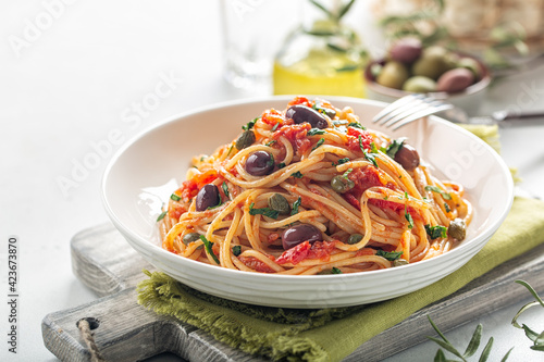 Italian lunch. Spaghetti alla puttanesca - italian pasta dish with tomatoes, olives, capers and parsley. Light background. Copy space. photo