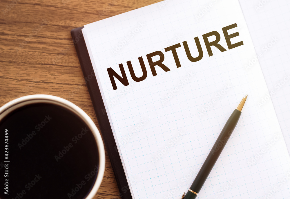 NURTURE - text on notepad on wooden desk. NURTURE - text on notepad on wooden desk.