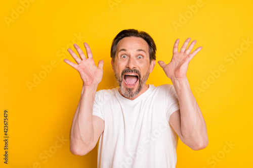 Photo of crazy excited man open mouth raise palms look camera wear white t-shirt isolated yellow background