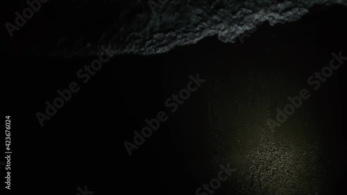 A man emerges from the water at night in a spot of light against the background of the white foam of the sea surf. View from above