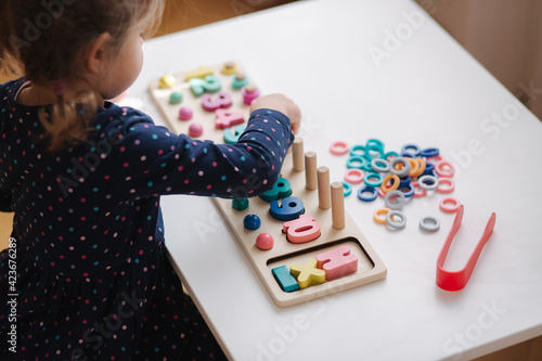 Adorable little girl play in educational game for children at the table. Wooden game with different colors and numbers. Intecactive game for smart kids. Girl spent time at home during quarantine