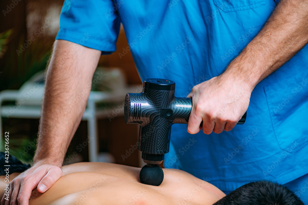 Massage Gun Physical Therapy Treatment. Physical Therapist Massaging Man’s Back