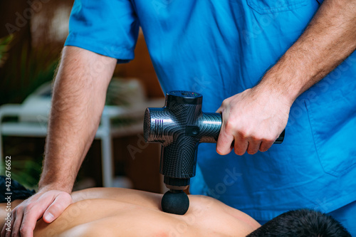 Massage Gun Physical Therapy Treatment. Physical Therapist Massaging Man   s Back