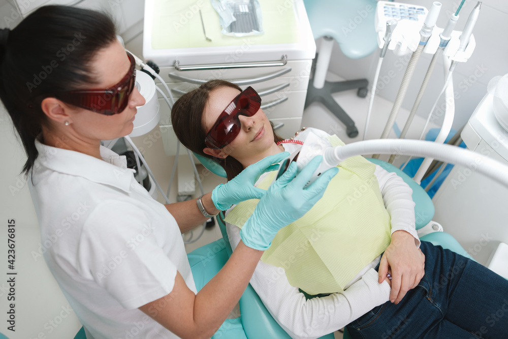 Young woman getting teeth whitened by professional dentist at the clinic Young woman getting teeth whitened by professional dentist at the clinic