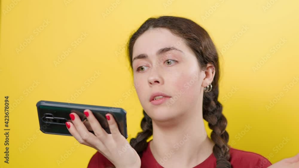 A young beautiful brunette woman is talking on a smartphone, recording a voice message in the app. Yellow background. Communication concept. A young beautiful brunette woman is talking on a smartphone, recording a voice message in the app. Yellow background. Communication concept.
