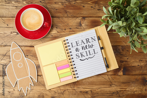 Learn new skill text on notebook on wooden table with coffee cup and paper rocket. Business concept of positive thinking and motivation