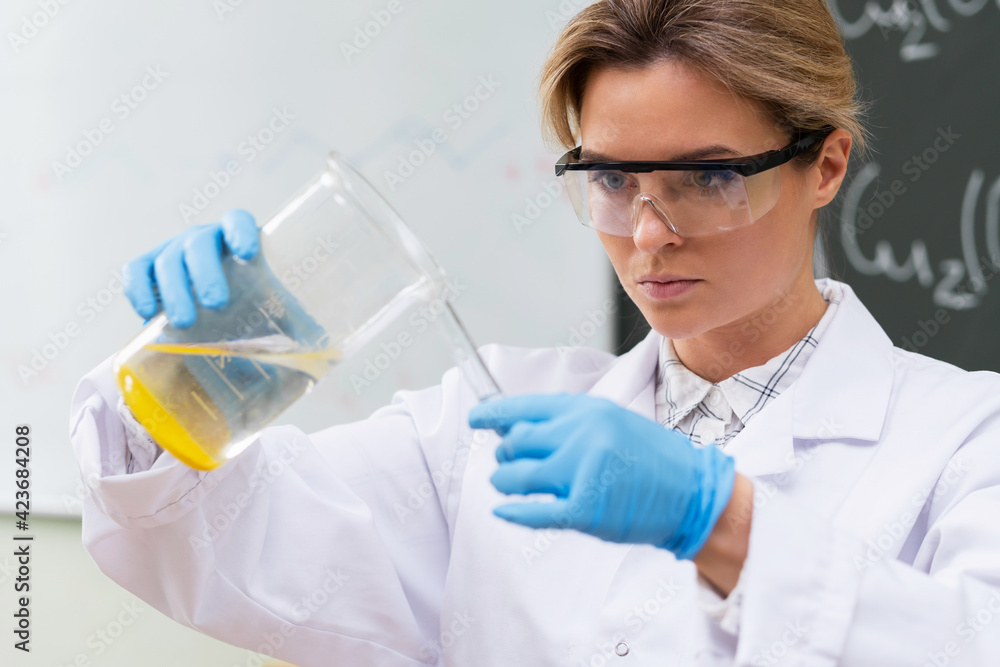 Scientist pouring substance from beaker to test tube in a laboratory during research Scientist pouring substance from beaker to test tube in a laboratory during research