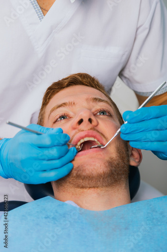 Smiling young man sitting in dentist chair while doctor examining his teeth.