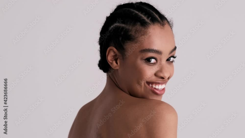 A back view of a smiling young half-naked woman is turning to the camera standing isolated over a gray background in the studio A back view of a smiling young half-naked woman is turning to the camera standing isolated over a gray background in the studio