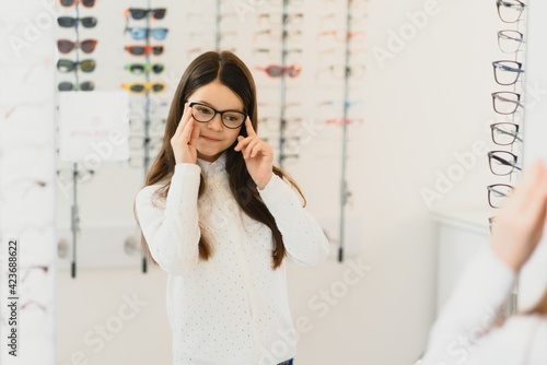 Health care, eyesight and vision concept - happy woman choosing glasses at optics store. Portrait of beautiful young woman trying new glasses in optician store