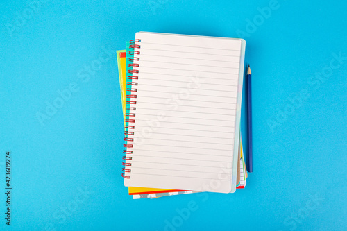 school notebooks on a blue background, spiral notepad with a blank page and a pencil on the table top view