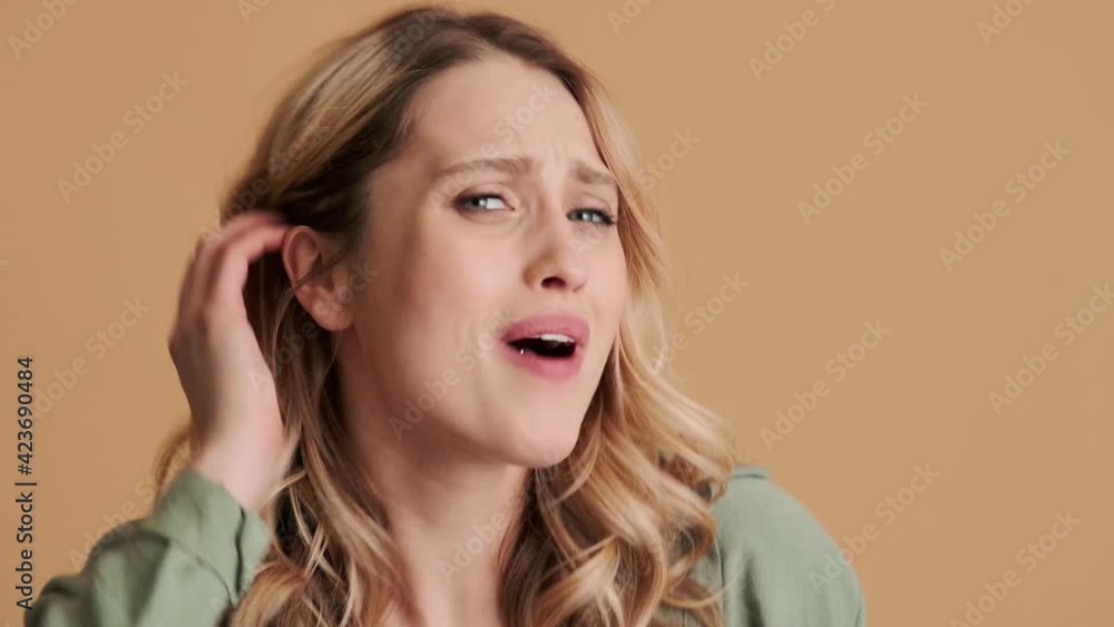 A close-up view of a displeased young woman is gesturing to the camera negatively standing isolated over beige background in studio A close-up view of a displeased young woman is gesturing to the camera negatively standing isolated over beige background in studio