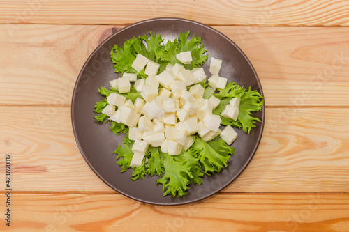 Diced soft cheese on lettuce leaves on dish, top view