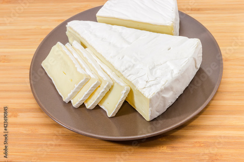 Pieces of brie cheese on brown dish on wooden surface