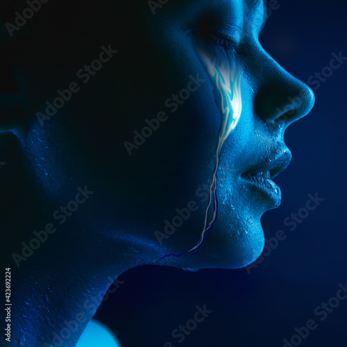 Portrait of young beautiful woman with neon, fluid tears from eyes. Concept of fashion and beauty, emotions and feelings, modern design