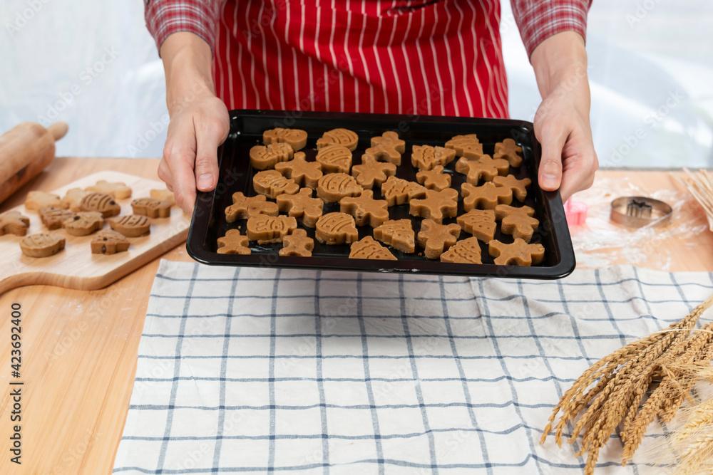 Young male baking cookies in kitchen at home. Male making Christmas cookies in many shape on a wooden board. Young man cooking cookies in kitchen. Making homemade shortbread cookies. Young male baking cookies in kitchen at home. Male making Christmas cookies in many shape on a wooden board. Young man cooking cookies in kitchen. Making homemade shortbread cookies.