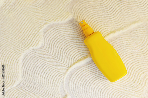 yellow cosmetic bottle with sunscreen cream spray on sand textured background. Cosmetic products  with spf. UV protection concept. Copy space