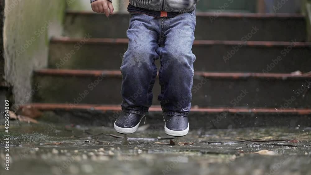Child jumping into puddle in slow-motion. Toddler jumps into water Child jumping into puddle in slow-motion. Toddler jumps into water