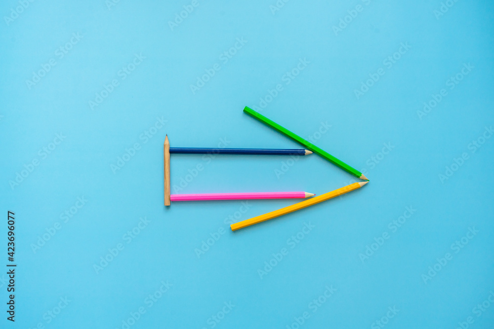 Ein Pfeil aus Buntstiften auf einem blauen Hintergrund. Flat lay, Kreativität. Ein Pfeil aus Buntstiften auf einem blauen Hintergrund. Flat lay, Kreativität.