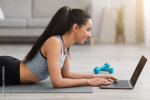 Side view of lady laying on fitness mat, using laptop