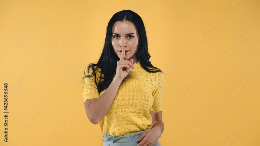 brunette woman looking at camera while showing hush sign isolated on yellow brunette woman looking at camera while showing hush sign isolated on yellow