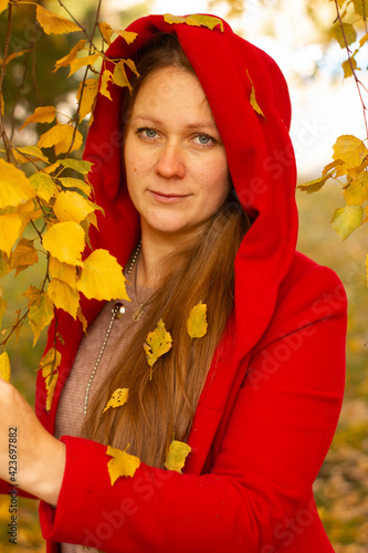 Young beautiful sexy girl in a red coat in the autumn forest among the yellow foliage