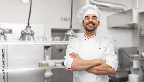 cooking, culinary and people concept - happy smiling male chef in toque and jacket over restaurant kitchen background