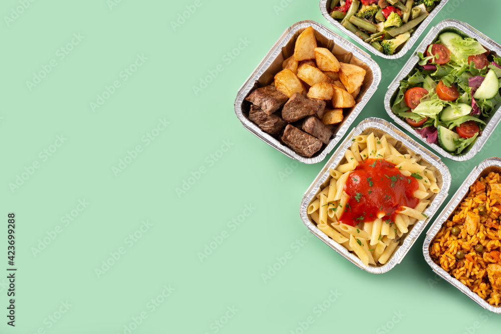 Take away healthy food in foil boxes on green background. Copy space - obrazy, fototapety, plakaty 