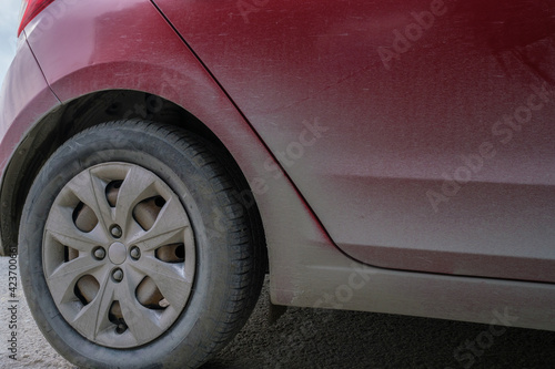 detail of right back wheels of red car automobile in dust and dirt on sides before cleaning and washing