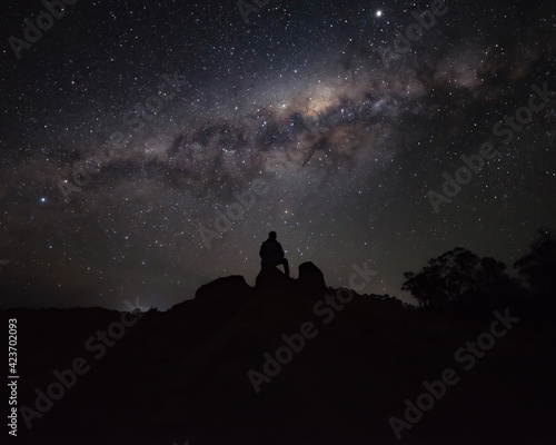 Silhouette of a Person Sitting on a Rock Watching the Milky way © nicolas