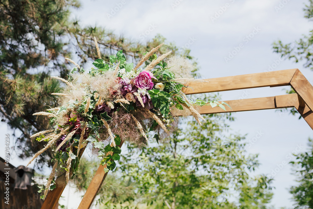 Close-up of flowers and greenery on a beautiful wooden wedding arch. Preparing for the wedding event in the forest.