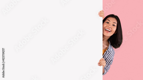 Obraz na plátně Asian woman hiding behind blank white advertising billboard