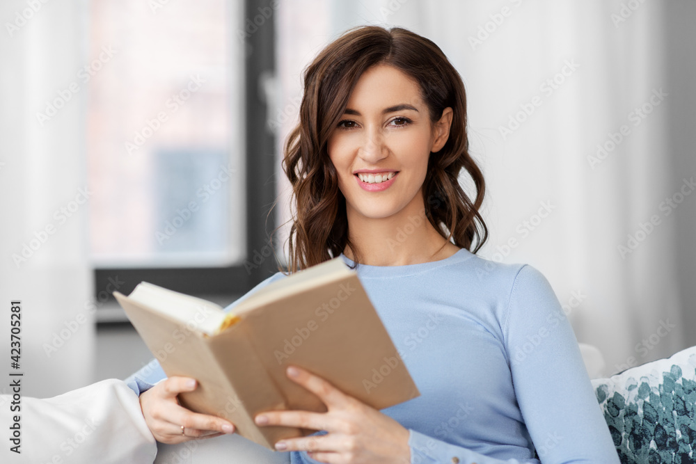people and leisure concept - happy young woman sitting on sofa and reading book at home people and leisure concept - happy young woman sitting on sofa and reading book at home