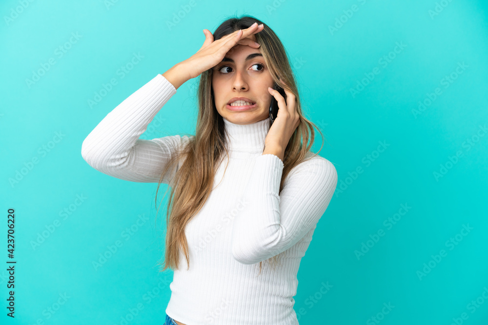 Young caucasian woman using mobile phone isolated on blue background doing surprise gesture while looking to the side