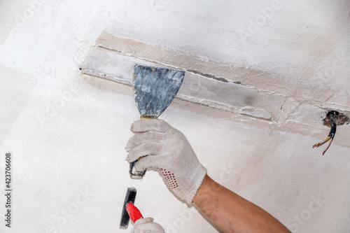 mans hand in cloth glove with spatula and putty, applies mastic to the wall, ceiling to level the surface. The process of applying mastic withspatula to the surface for interior design of the room.