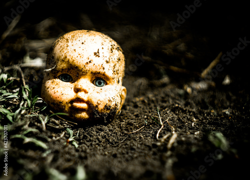 Old broken scary doll head on a ground in abandoned village.
