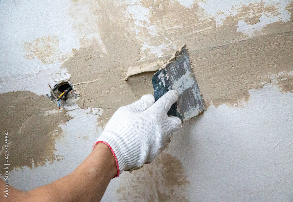 mans hand in cloth glove with spatula and putty, applies mastic to the