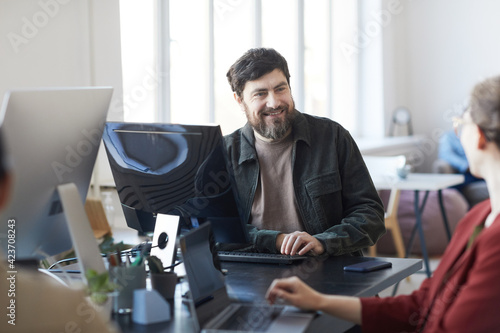 Portrait of smiling bearded man talking to colleagues during meeting in modern IT office, copy space