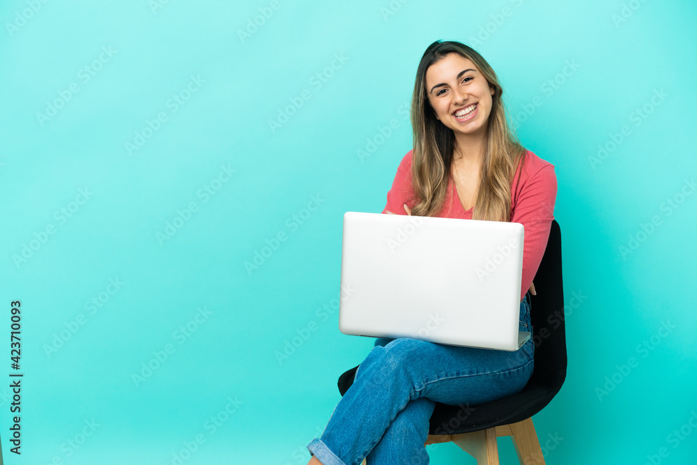 Young caucasian woman sitting on a chair with her pc isolated on blue background with arms crossed and looking forward Young caucasian woman sitting on a chair with her pc isolated on blue background with arms crossed and looking forward