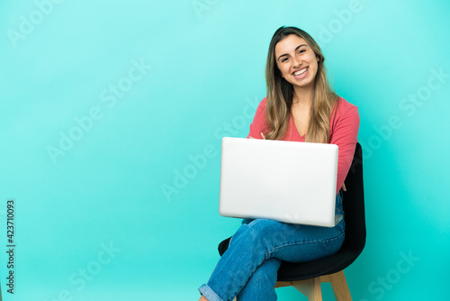 Young caucasian woman sitting on a chair with her pc isolated on blue background with arms crossed and looking forward © luismolinero