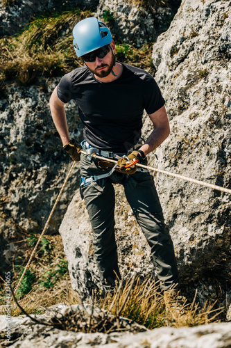 Young man rappelling down a rocky cliff, he is attached on rope with a figure eight and carabiner. Extreme adventure in the mountains.