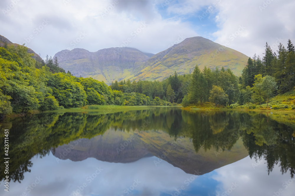 Idyllic, lush and green mountain landscape reflection on a calm Torren Lochan on a summer day at Glencoe in the Scottish Highlands, Scotland.