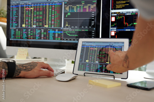 Close-up image of trader checking stock market data on screens of computer and tablet computer