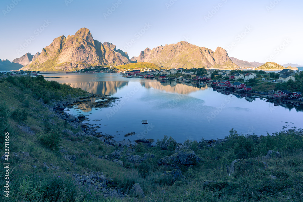 Village of Reine in Lofoten in the golden hour during sunset. Rocks and the village reflect on the water surface. Beautiful evening in the arctic. Sunset in norwegian fjord.