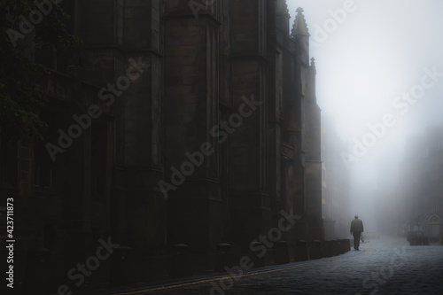 Silhouette of a man walking beside St Giles' Cathedral in moody atmospheric old town Edinburgh along the cobblestone Royal Mile in misty fog.
