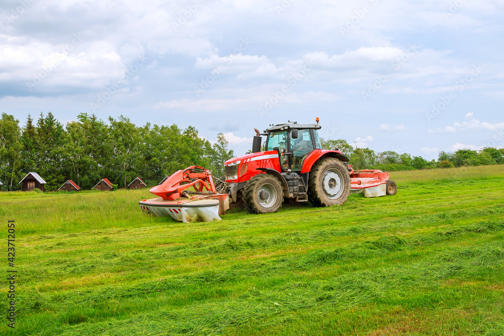 Big red tractor with two mowers mows the grass for silage Big red tractor with two mowers mows the grass for silage